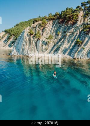 Mann auf Stand-Up-Paddle-Board in blauem Meer. Surfer auf dem SUP-Board im Mittelmeer mit Berglandschaft. Luftaufnahme Stockfoto