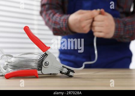 Professioneller Elektriker zum Abisolieren von Drähten und Schneidern auf Holztischen in Innenräumen, selektiver Fokus Stockfoto