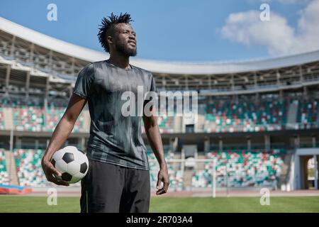 Ein junger Mann steht in einem Stadion mit einem Fußball in der Hand Stockfoto