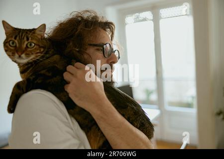 Der gutaussehende junge Tierliebhaber umarmt die Katze während der Ruhezeit zu Hause Stockfoto