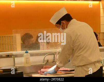 Sushi-Koch filetiert frischen Thunfisch im Kaiten Sushi Restaurant in Tokio, Japan. Stockfoto