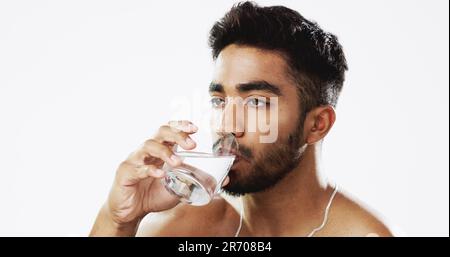 Mensch trinkt Wasser, Hydratation und Gesundheit mit ernstem Gesicht und Glas in der Hand isoliert auf weißem Hintergrund. Durstiger Indianer, männlich im Studio, H2O und Stockfoto