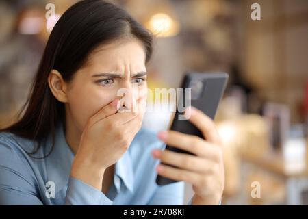 Verängstigte Frau, die sich Medieninhalte am Telefon in einem Restaurant ansieht Stockfoto