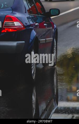 Ein silbernes Auto parkt auf einer nassen Straße und spiegelt sich in der Dämmerung in einer Pfütze wider Stockfoto