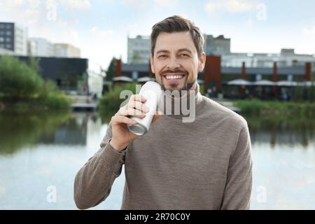 Glücklicher Mann, der eine Blechdose mit einem Getränk in der Nähe des Flusses im Freien hält Stockfoto