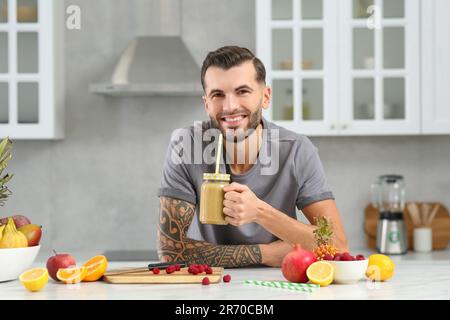 Hübscher Mann mit leckerem Smoothie am weißen Tisch in der Küche Stockfoto