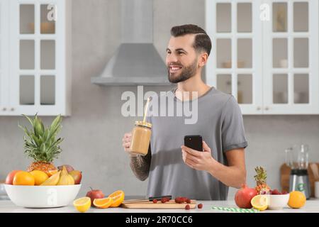 Hübscher Mann mit leckerem Smoothie in der Küche. Platz für Text Stockfoto