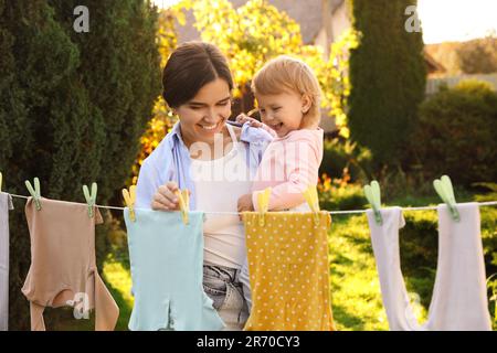 Mutter und Tochter hängen Kleidung mit Wäscheklammern an der Wäscheleine zum Trocknen im Garten Stockfoto