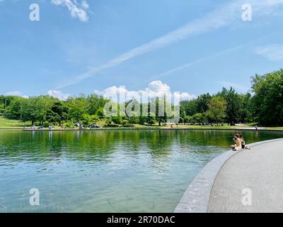 Der Blick auf den Beaver Lake Fountain Park mit zwei Frauen, die am Ufer sitzen. Stockfoto