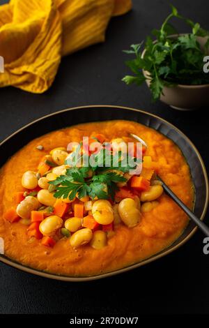 Gesundes Mittagessen, Tomaten- und Karottensuppe, Bohnen mit Kürbiskernen, gesunde, leckere Hülsenfrüchte, Blick auf einen Teller Suppe auf schwarzem Hintergrund Stockfoto