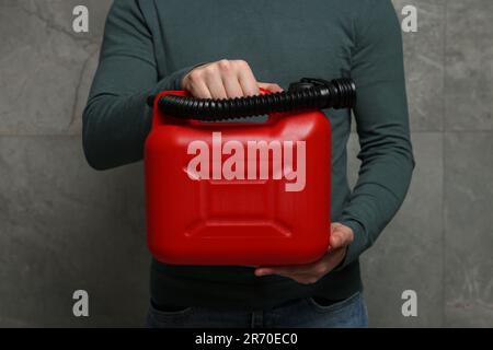 Ein Mann hält einen roten Kanister nahe der grauen Wand, Nahaufnahme Stockfoto