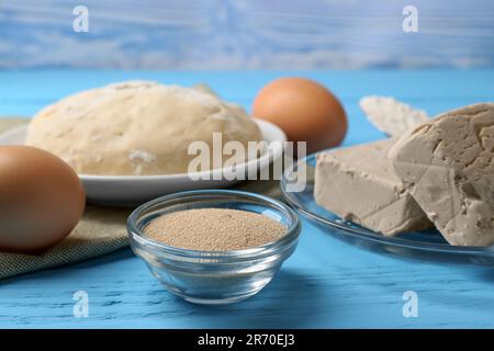 Verschiedene Arten von Hefe, Eiern, Teig und Mehl in Löffel auf hellblauem Holztisch Stockfoto