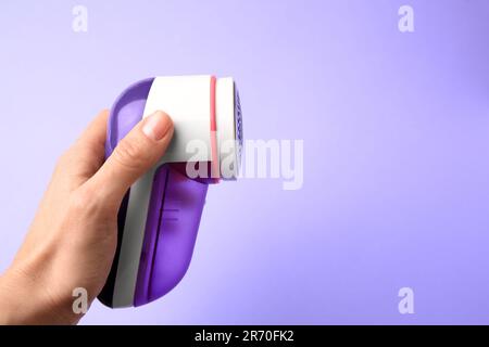Eine Frau, die einen modernen Stoffrasierer auf violettem Hintergrund hält, Nahaufnahme. Platz für Text Stockfoto