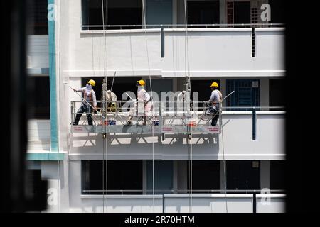 Arbeiter, die einen Industrieleiter benutzen, der in der Luft hängt und unter der heißen Sonne einen Gebäudeaußenbereich lackiert. Ein sehr risikoreicher Beruf. Stockfoto