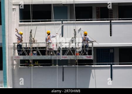 Arbeiter, die einen Industrieleiter benutzen, der in der Luft hängt und unter der heißen Sonne einen Gebäudeaußenbereich lackiert. Ein sehr risikoreicher Beruf. Stockfoto