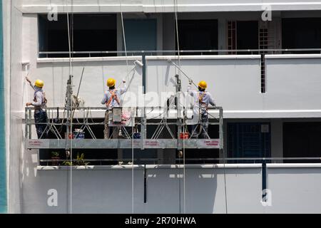 Arbeiter, die einen Industrieleiter benutzen, der in der Luft hängt und unter der heißen Sonne einen Gebäudeaußenbereich lackiert. Ein sehr risikoreicher Beruf. Stockfoto