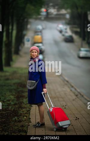 Eine Frau mit einem roten Koffer läuft die Straße hinunter. Stockfoto