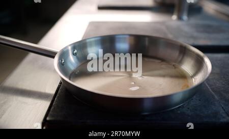 Der Koch gießt Öl in eine heiße Pfanne in einer professionellen Küche, die in einem Restaurant kocht. Nahaufnahme eines Kochs, der Öl in eine Pfanne gießt. Stockfoto