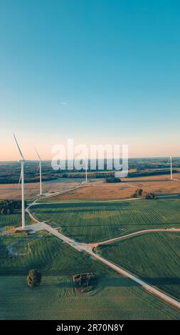 Ein malerischer Blick auf ein üppiges grünes Feld mit großen Windturbinen vor einem wunderschönen blauen Himmel. Stockfoto