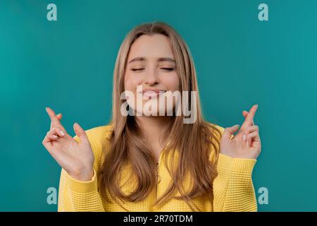 Hübsche Frau betet mit gedrückten Fingern auf blauem Hintergrund. Wünsche  befriedigen Stockfotografie