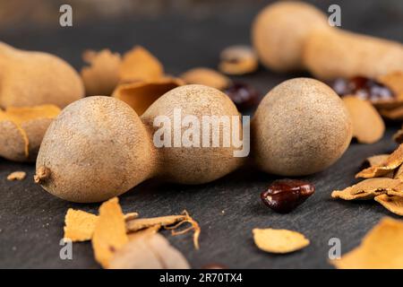 Geschlossene, lange reife Tamarindenschoten aus der Nähe, verzehrfertige ganze Tamarindenfrüchte liegen auf dem Tisch Stockfoto