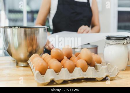 Hähnchenei mit Zutaten zum Backen auf dem Tisch mit weiblicher Bäckerin im Hintergrund. Stockfoto