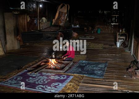 Einheimische Frau sitzt am Feuer in einem traditionellen Langhaus aus Bambus eines Nyishi-Stammes in Arunachal pradesh, Indien Stockfoto