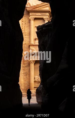 Silhouette einer Frau vor der wunderschönen Al Khaznov (Schatzkammer), die durch die Wände eines Canyons in Petra gesehen wird. Stockfoto