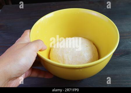 Die Hand des Mannes legt eine Schüssel mit Knete auf den Tisch, damit er vor dem Backen aufsteht Stockfoto