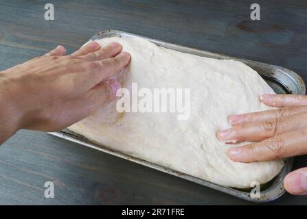 Die Hände strecken den Teig in einem Topf, um Pizza zu backen Stockfoto