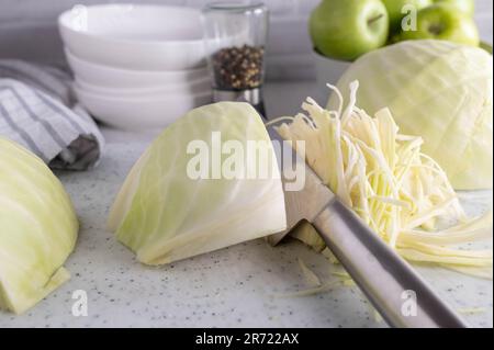 Gehackter Weißkohl auf einem Schneidebrett auf dem Küchentisch mit Zerkleinerer-Messer. Stockfoto