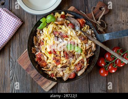 Pasta mit geröstetem Hühnerfleisch, Tomaten, Zwiebeln, Knoblauch und Kräutern in einer Pfanne auf einem Holztisch Stockfoto