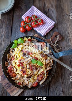 Pasta mit geröstetem Hühnerfleisch, Tomaten, Zwiebeln, Knoblauch und Kräutern in einer Pfanne auf einem Holztisch Stockfoto