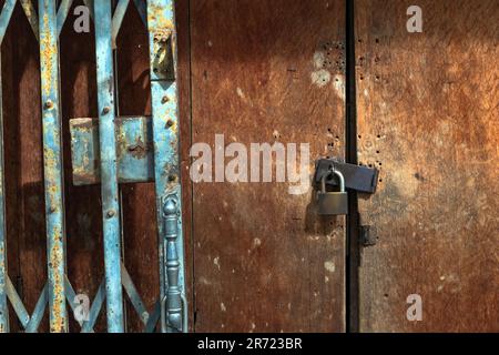 Altes goldenes Stahlschloss und beschädigte und verrostete Stahltür an Holztür. Verriegelt an Holztür mit altem Metallladen und Falttor. Alter Arbeitsauftrag Stockfoto