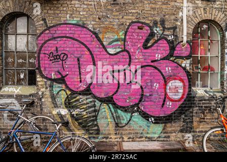 Kopenhagen, Dänemark - 14. September 2010: Christiania freetown. Großes rosa Graffiti auf brauner Backsteinwand des alten Lagerhauses. Fahrräder vor dem Hotel Stockfoto