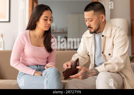 Ein Unglückliches Asiatisches Paar, Das Sich Wallet Mit Finanzproblemen Im Haus Ansieht Stockfoto