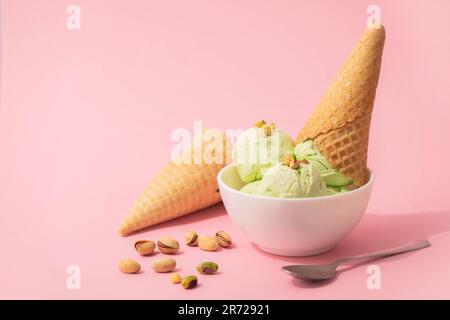 Pistazieneis in einer weißen Schüssel und Waffelform, rosa Hintergrund, Kopierbereich. Sommerliche kühlende Desserts Stockfoto