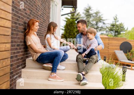 Familie mit einer Mutter, einem Vater, einem Sohn und einer Tochter, die draußen auf den Stufen einer Veranda eines Backsteinhauses sitzen Stockfoto