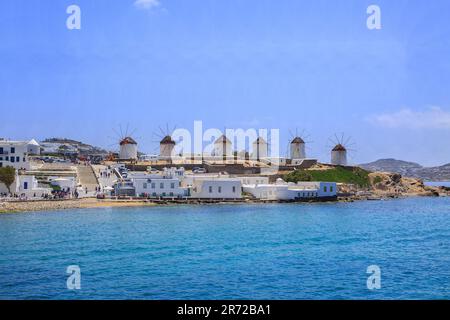 Landschaftsblick auf die berühmten weißen Windmühlen auf der Insel Mykonos, mit dem Ägäischen Meer, das darunter glitzert. Stockfoto