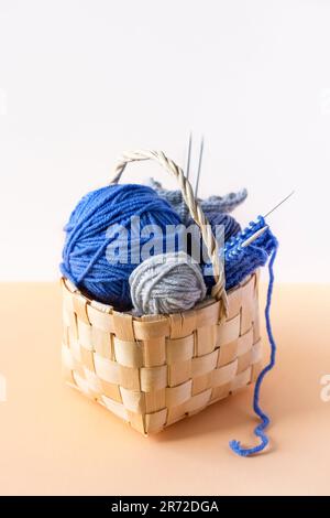 Blaue Strickgarnkugeln auf gelbem Hintergrund in einem Korb mit Stricknadeln Stockfoto