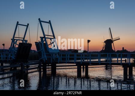 Zugbrücke am Fluss, Kanal und wunderschöner Sonnenuntergang. Holzwindmühlen bei Sonnenuntergang im holländischen Dorf Kinderdijk. Windmühlen laufen auf dem Wind. Die BEA Stockfoto