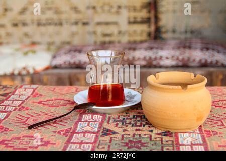 Foto in der Türkei. Das Bild zeigt ein kleines Glas starken Tee, genannt - Panzer auf einem traditionellen türkischen Teppich auf dem Tisch. In der Nähe eines Topfs Stockfoto