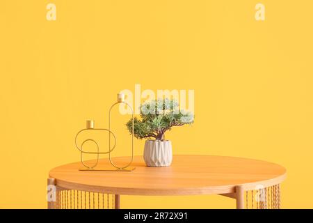 Hölzerner Kaffeetisch mit Bonsai-Baum und dekorativen Kerzenhaltern in der Nähe der orangefarbenen Wand Stockfoto