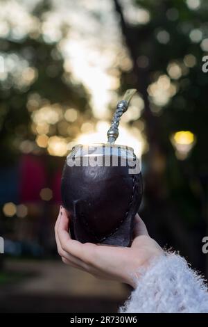 Eine Nahaufnahme der Hand der Frau, die einen schwarzen Mate-Becher mit Mate Bombilla hält. Stockfoto