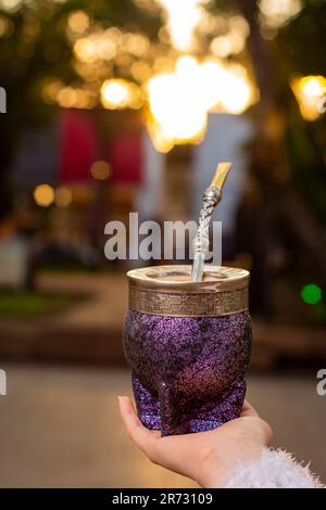 Eine Nahaufnahme der Hand der Frau, die eine lila Mate-Tasse mit Mate Bombilla hält. Stockfoto