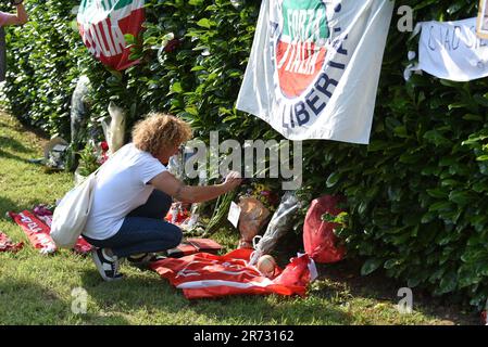 Monza, Italien. 12. Juni 2023. SILVIO BERLUSCONI, ehemaliger Premierminister, Medienmagnat und Fußballverein-Eigentümer, wurde im Alter von 86 Jahren von italienischen Medien für tot erklärt. In seiner Residenz in Arcore, einer kleinen Stadt in der Nähe von Monza, wollten Zehntausende ihm mit Blumen, Fußballmannschaftsflaggen und handschriftlichen Botschaften die Ehre erweisen.Ein Unterstützer überreicht Blumen in der Nachruf des ehemaligen Premierministers. (Kreditbild: © Ervin Shulku/ZUMA Press Wire) NUR REDAKTIONELLE VERWENDUNG! Nicht für den kommerziellen GEBRAUCH! Stockfoto