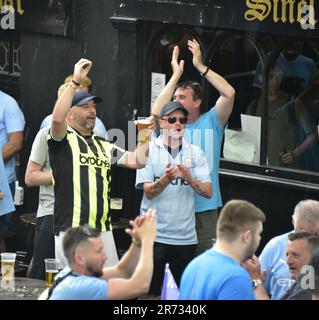 Manchester, Großbritannien. 12. Juni 2023. Fans genießen einen Drink, während sie warten, während der Manchester City Football Club sich auf eine Siegesparade mit offenem Oberdeck im Zentrum von Manchester, Großbritannien, vorbereitet, um die Erfolge des Sieges der Treble zu feiern: Die Premier League, der FA Cup und die Champions League. Am Samstag besiegte man City Inter Mailand in Istanbul und sicherte sich den Champions League-Sieg. Die Parade der offenen Busse fuhr durch das Stadtzentrum von Manchester und beobachtete von großen, begeisterten Massen, trotz Gewitter und starkem Regen. Kredit: Terry Waller/Alamy Live News Stockfoto