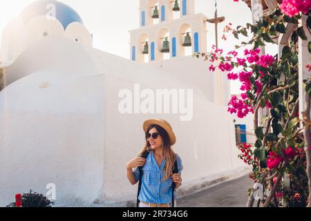 Santorini Tourist mit Rucksack Spaziergänge durch die Kirche mit blauer Kuppel und blühenden Bougainvillea Blumen in Akrotiri bei Sonnenuntergang. Sommerurlaub Stockfoto