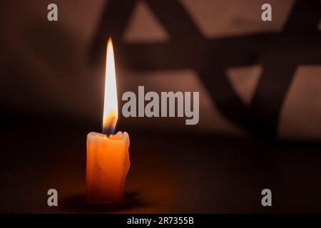 Holocaust-Gedenktag. Jom HaShoah. Leuchtende brennende Kerze und die offizielle Flagge Israels auf dunkelgrauem Hintergrund. Stockfoto