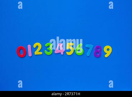 Bunte, helle Zahlen von 0 bis 9 auf blauem Hintergrund mit Kopierbereich. Mathematikfähigkeitskonzept. Flach liegend, Ansicht von oben für leuchtend farbige Zahlen mit Kopie sp Stockfoto